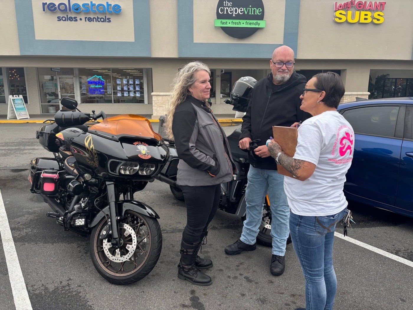 Cheryl Lucas meeting two customers in a car park, clipboard in hand, wearing a shirt with the Anytime Mobile Notary logo